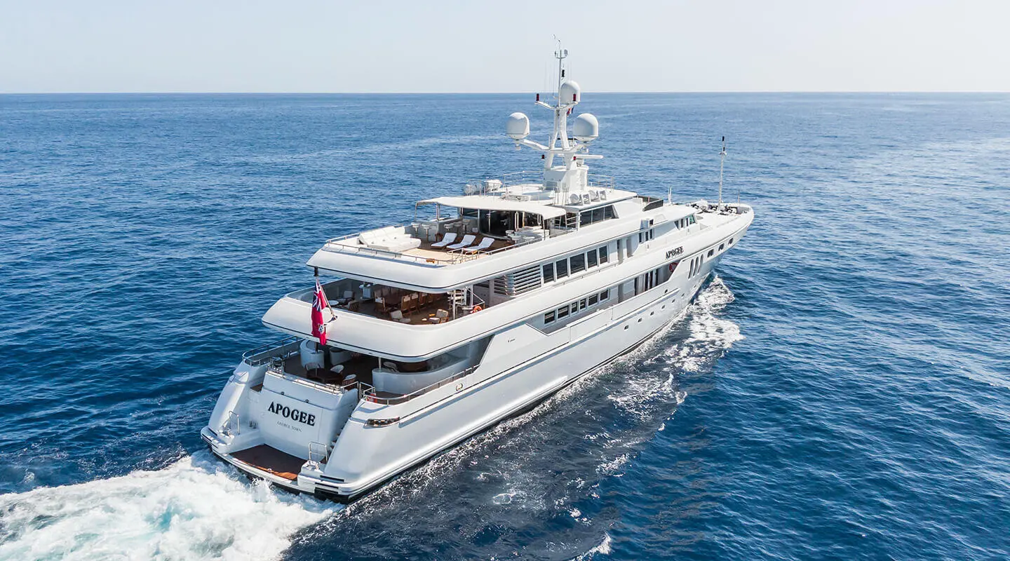 A white luxury motor yacht named Apogee sails on blue sea waters