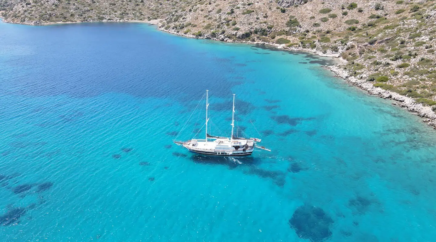 Two-masted gulet yacht anchored in turquoise blue water near rocky coastline