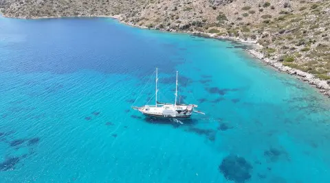 Two-masted gulet yacht anchored in turquoise blue water near rocky coastline