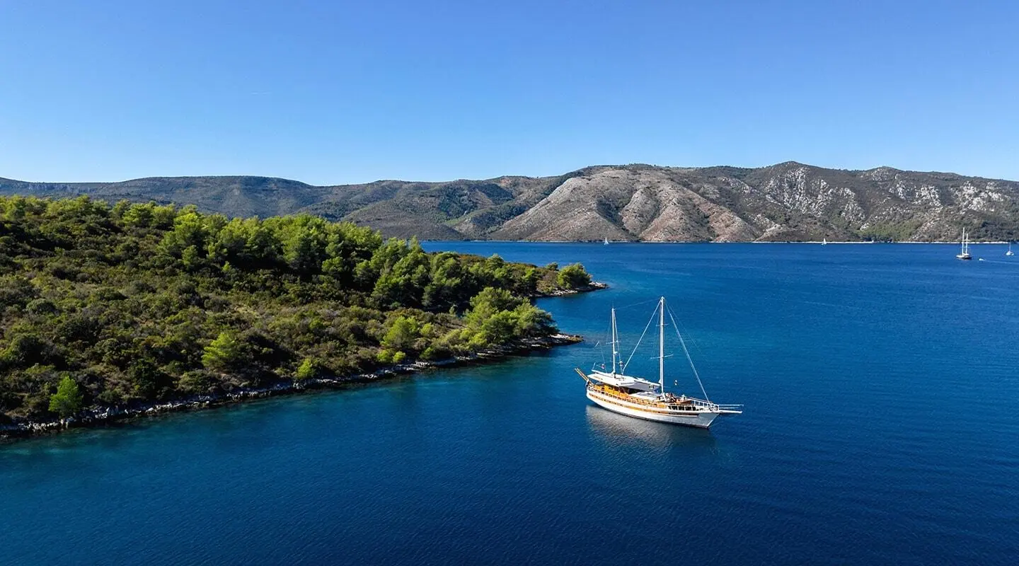 Yacht Aborda anchored in blue calm water near rugged coastline at sunset