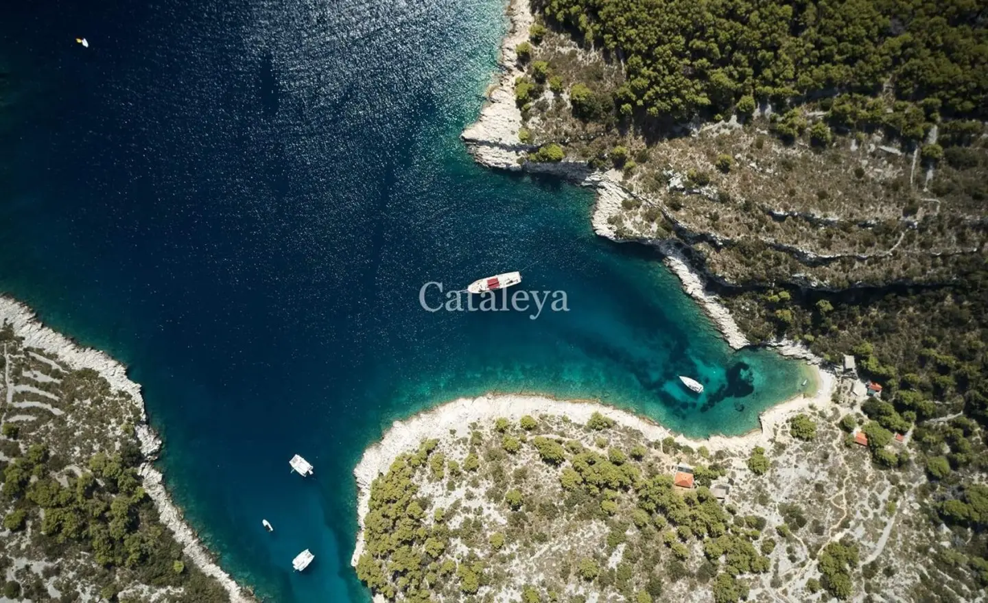 Aerial view of a turquoise cove with a red-and-white yacht near the rocky coastline