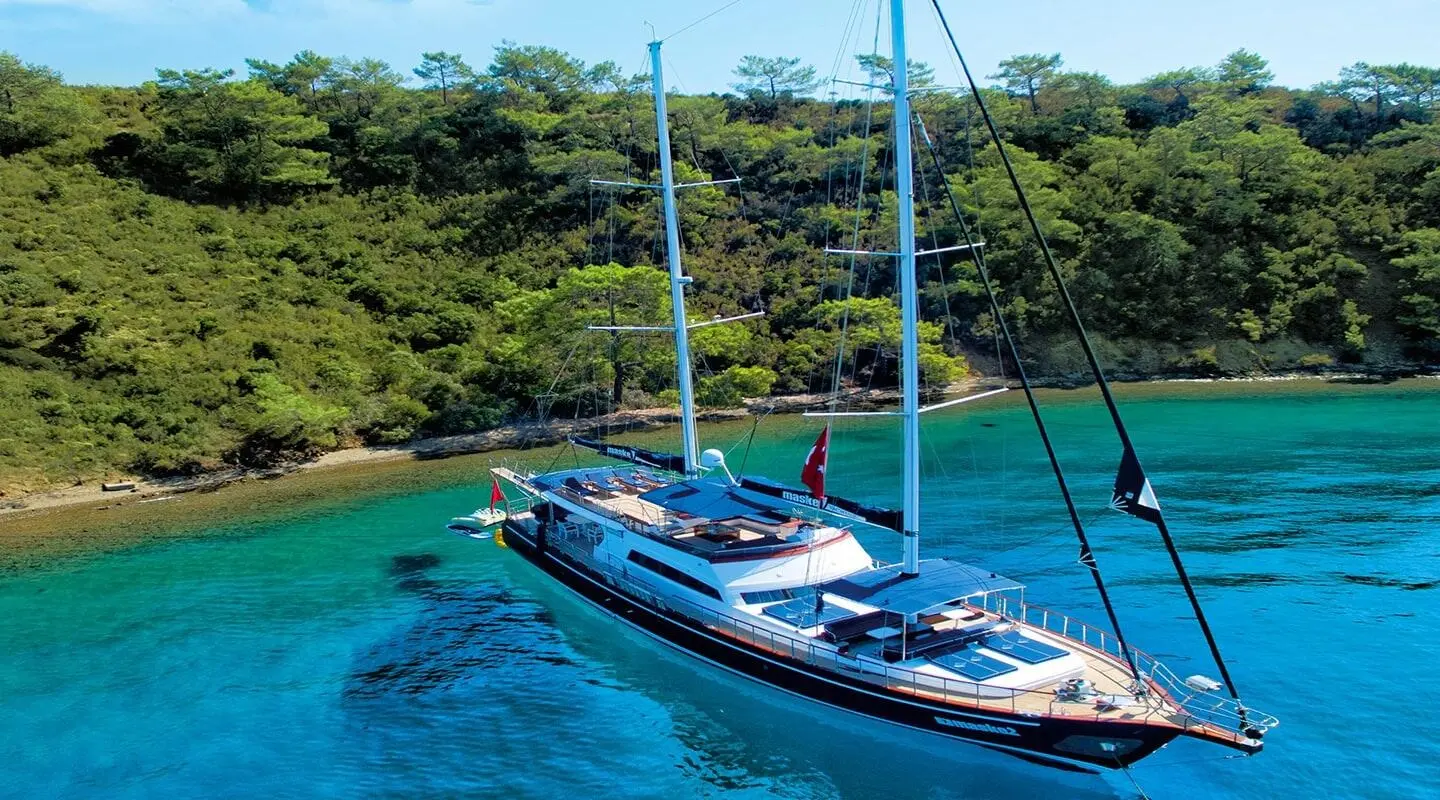 Maske 2 luxury gulet sailing at sunset with blue-tinted water and anchored near rocky coastline