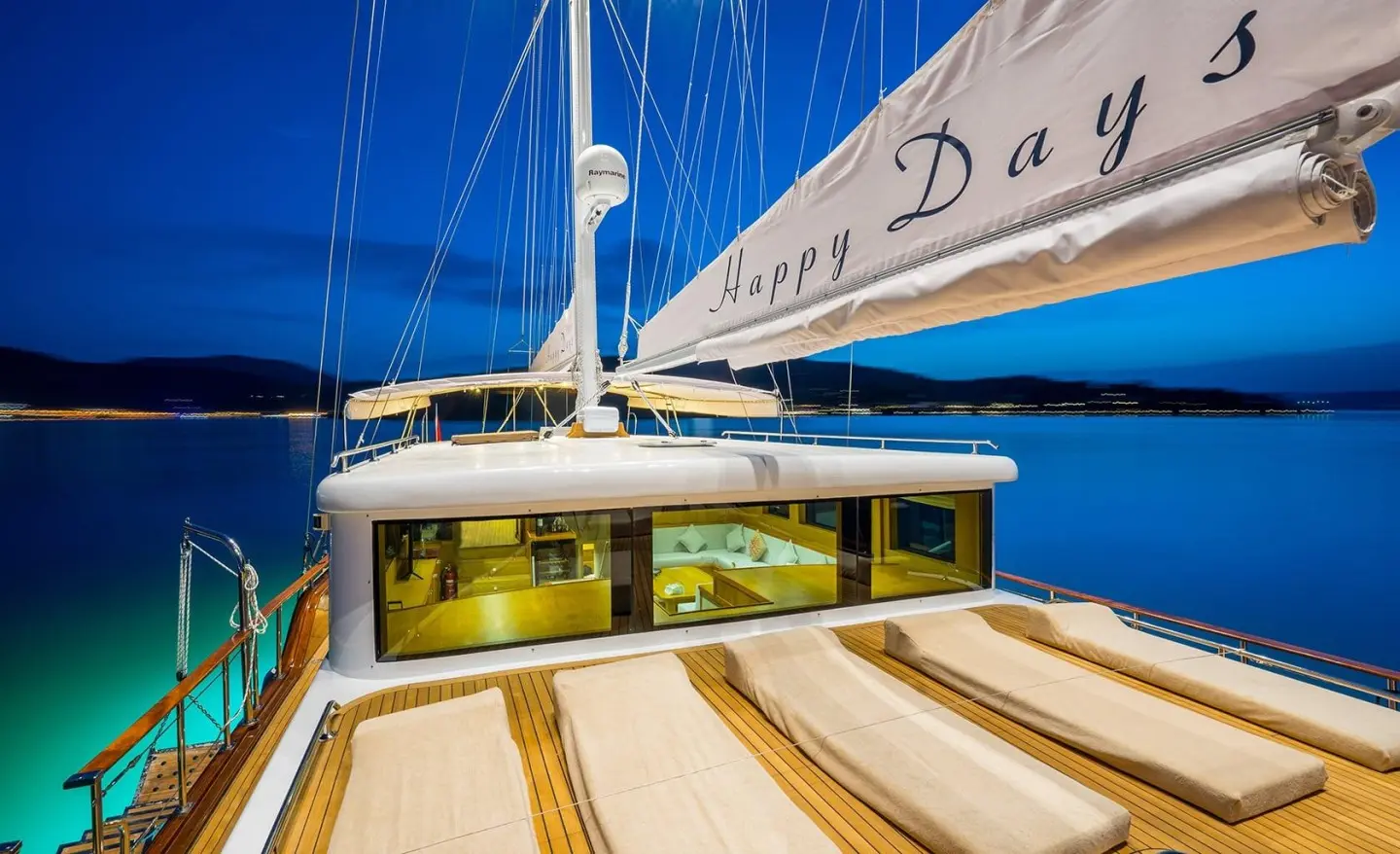 Close-up view of the yacht’s wooden deck and cabin under blue sail at sunset