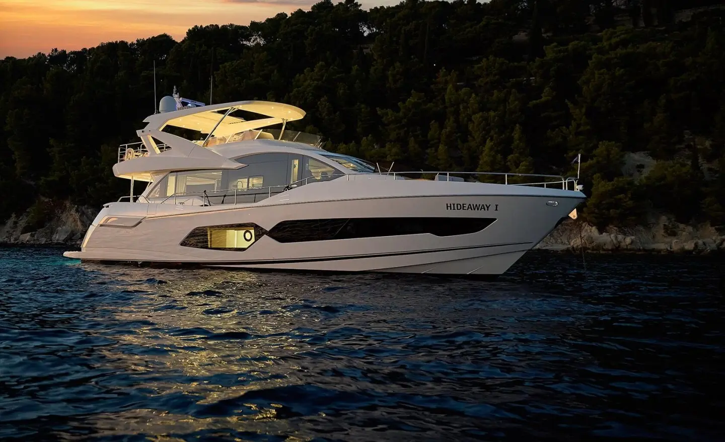 Sleek white yacht named Hideaway anchored on calm water at dusk