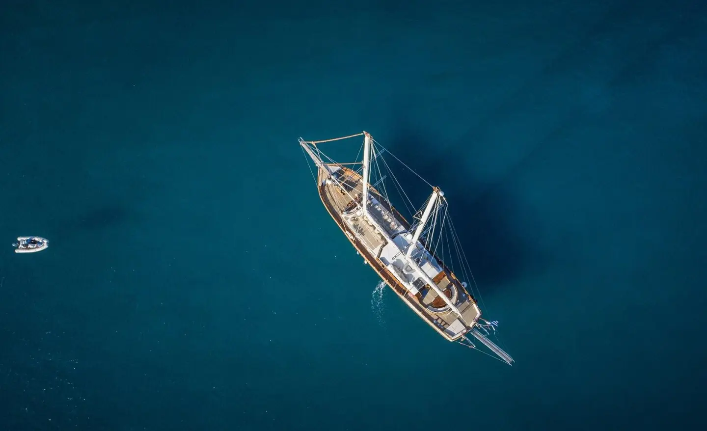 A small wooden yacht named Entre Cielos sails calm blue water at sunset