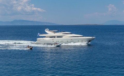 White luxury motor yacht speeding on the sea, with two small boats nearby