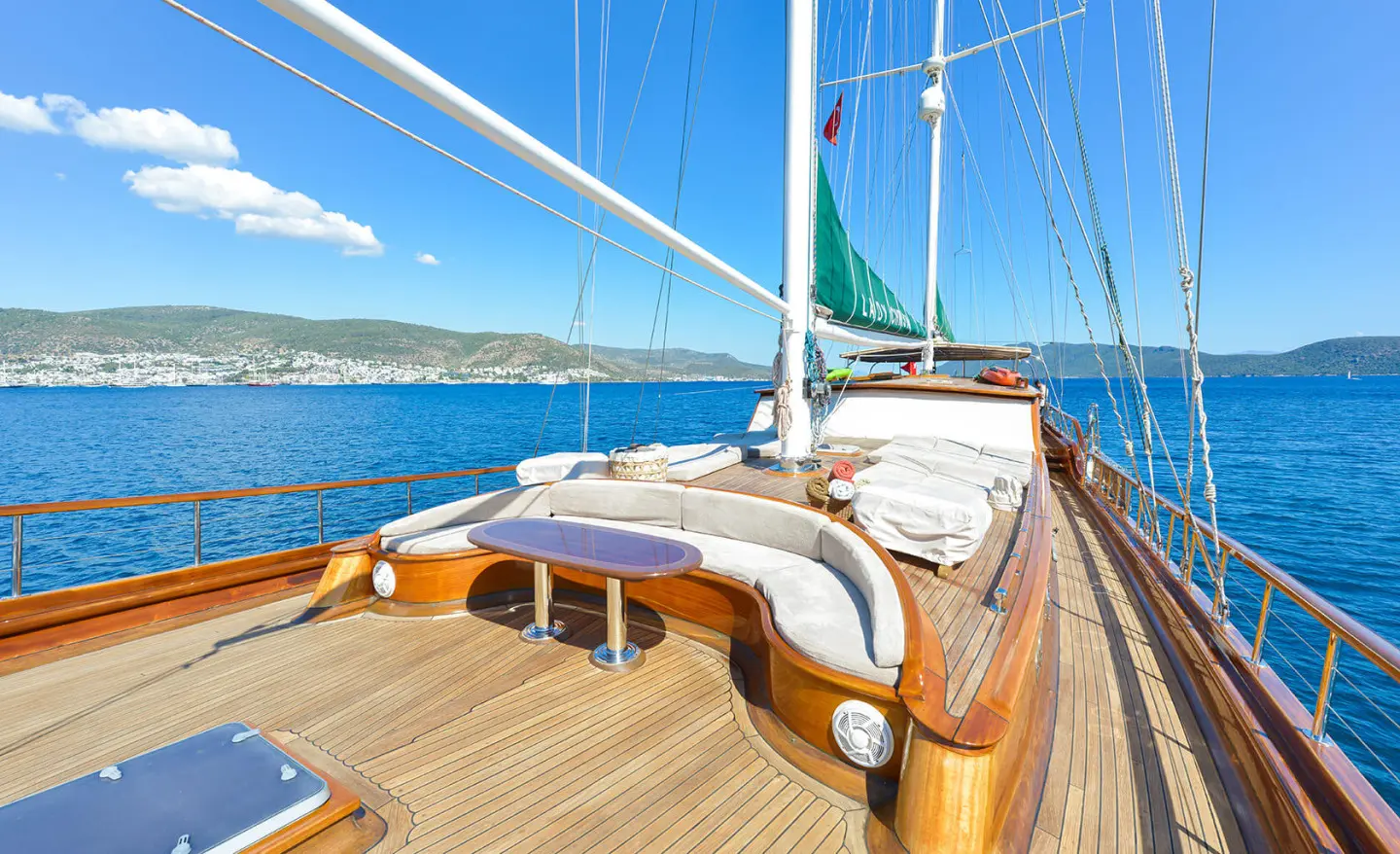 Lady Christa yacht deck with wooden railing, sails, and calm blue sea sunset