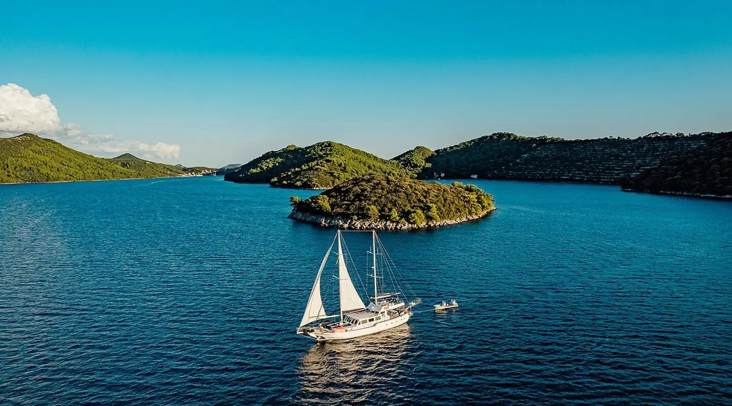 Maske yacht sails near small island at sunset over calm blue sea