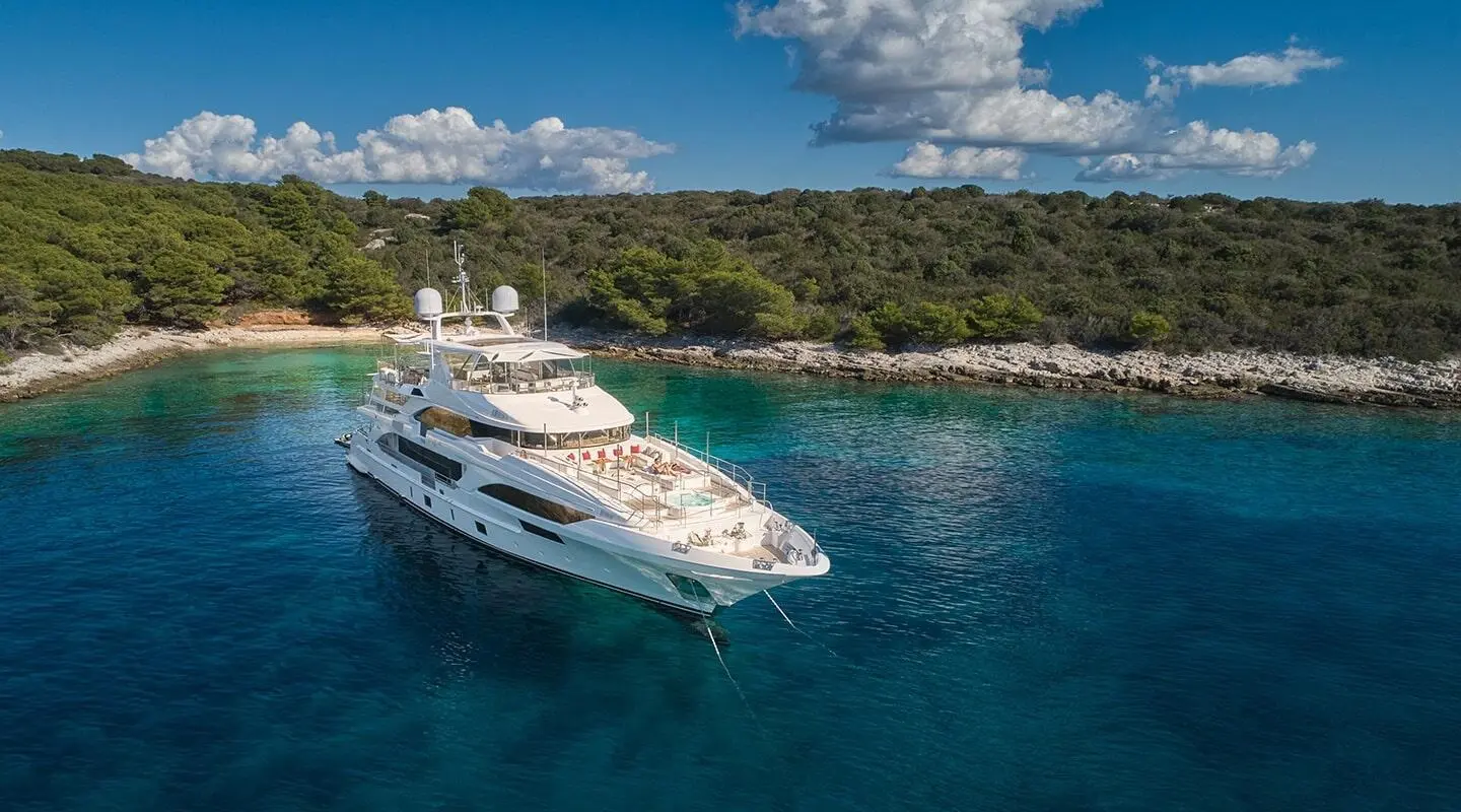 Happy Me yacht anchored in clear turquoise waters near a rocky shore with green trees