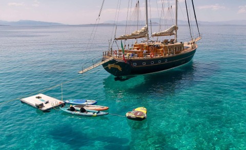 Myra yacht anchored in turquoise water with a wooden deck and sails, tender boats nearby