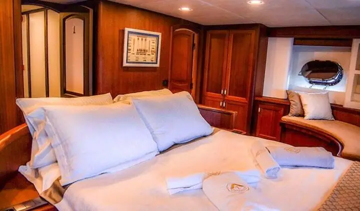 Master cabin with large bed, white linens, wooden panels, and built-in nightstands