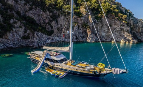 Luxurious sailing yacht anchored near rocky coastline in turquoise water