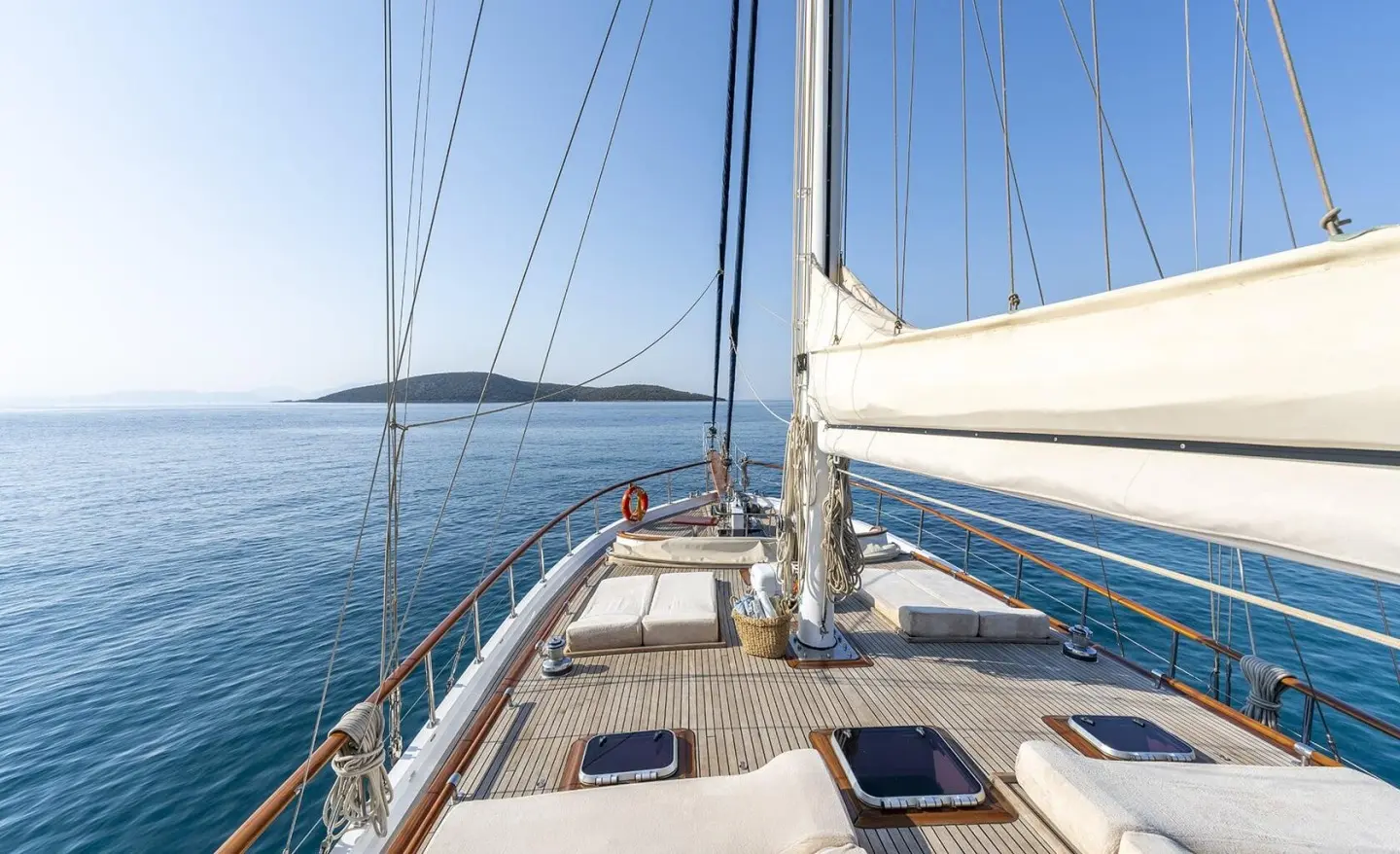 View of the yacht deck from the bow with ropes and masts against the blue sea