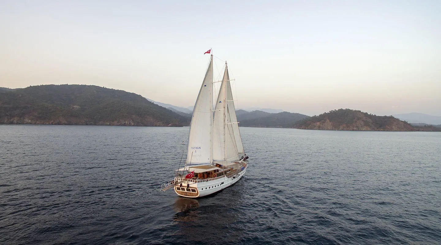 Kayhan 8 yacht sailing with white sails on calm sea at sunset