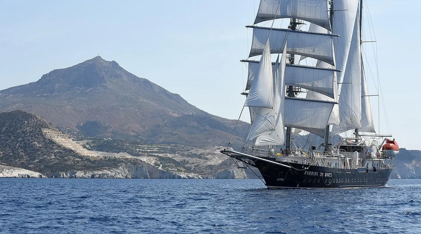 Sailing gulet with multiple masts on blue sea near rocky coastline