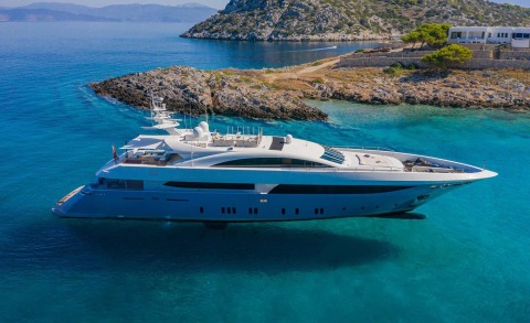 Large yacht anchored near rocky coastline with clear blue water.