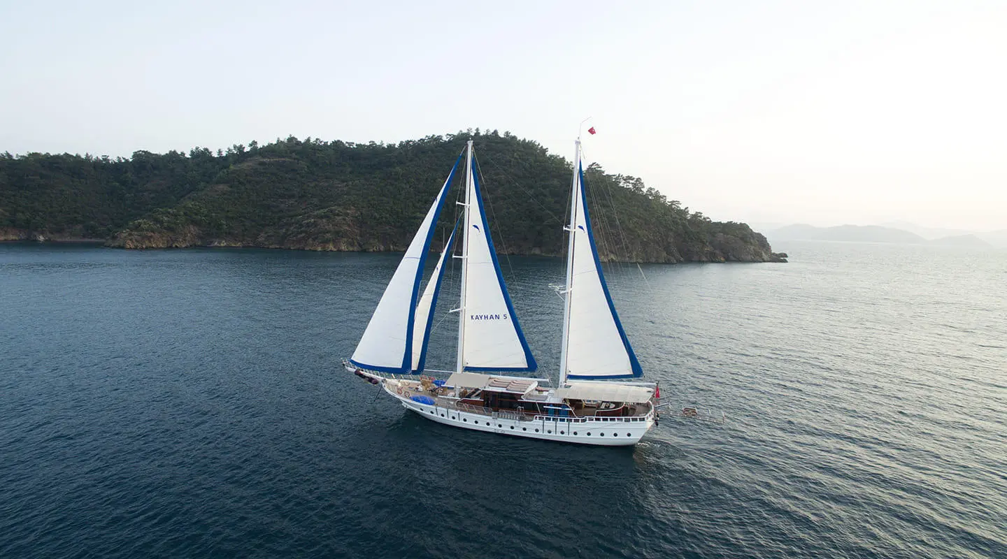 Kayhan 5 yacht sailing on calm blue water near rocky coastline at sunset