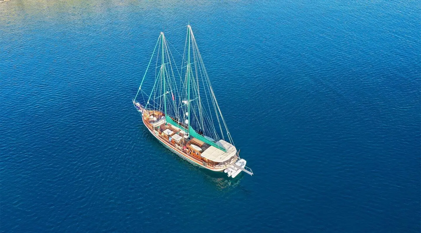 Yacht Ros Mare anchored in calm blue sea at sunset with sails furled