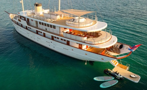 White luxury motor yacht with multiple decks anchored, visible upper deck seating and stairway