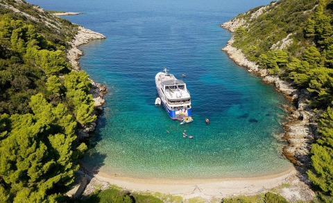 Lupus Mare yacht anchored in a turquoise bay, surrounded by green trees and rocky cliffs