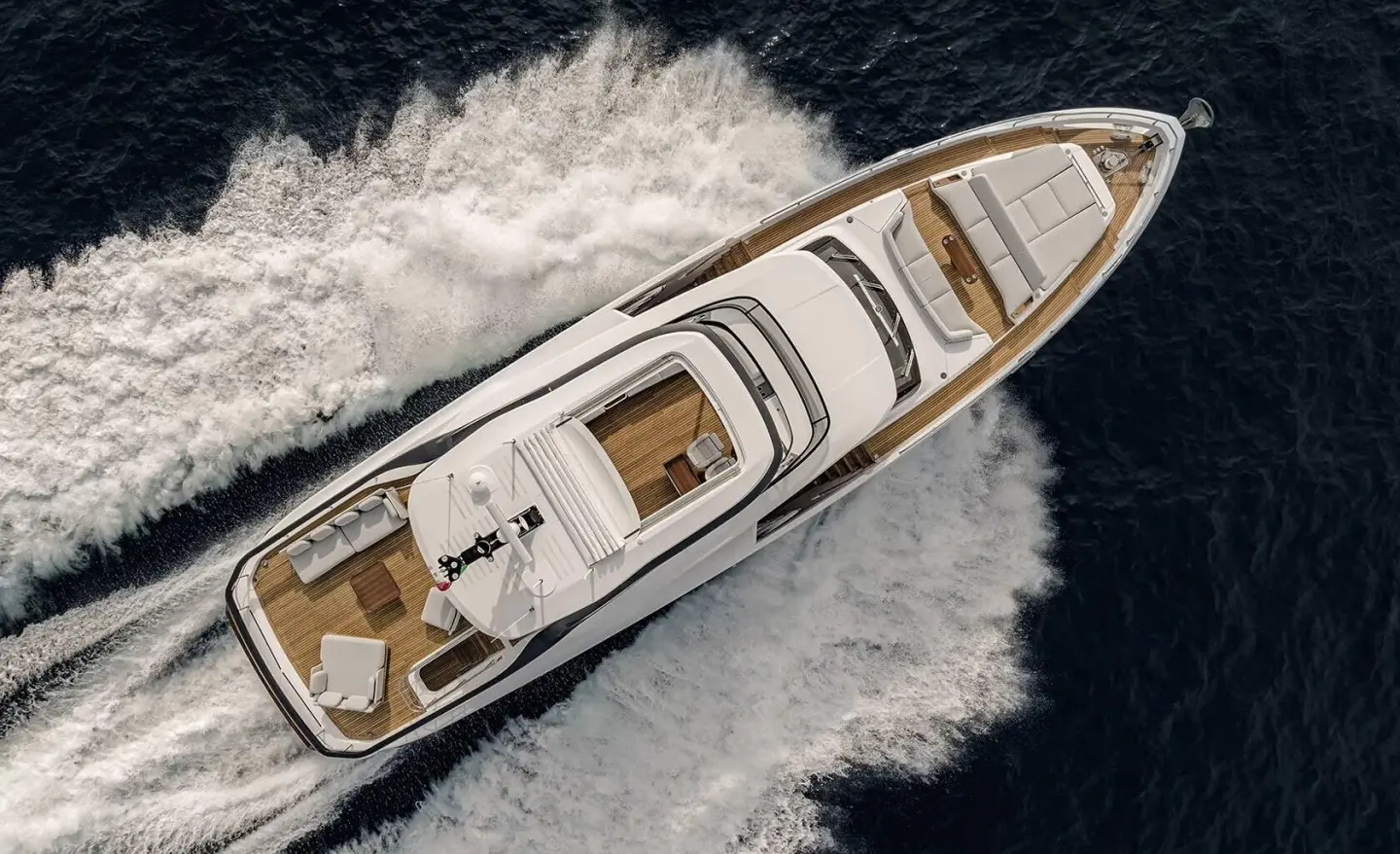 Top-down view of a sleek white yacht cutting through dark blue water near foamy wake