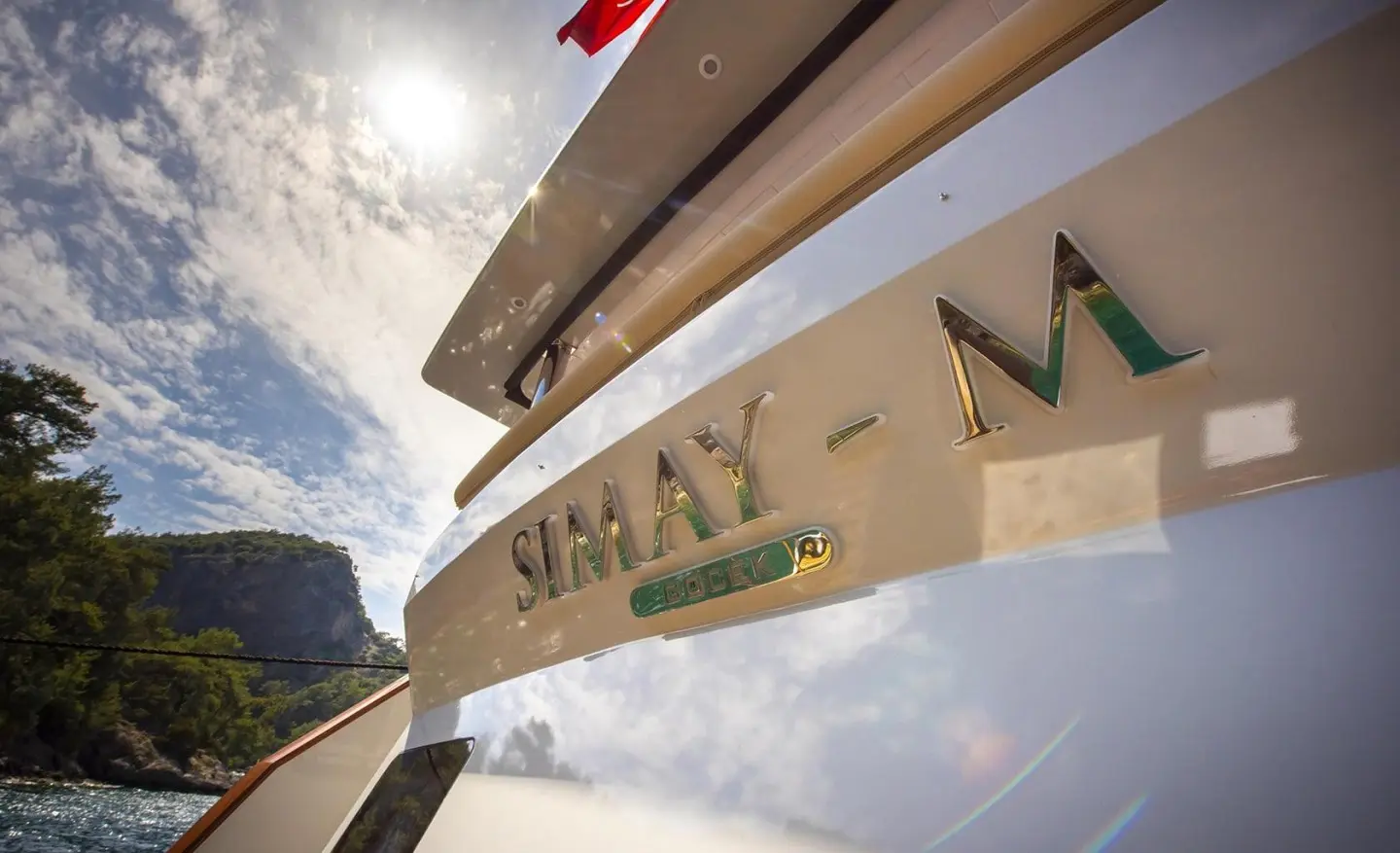 Close-up of the Simay M hull with chrome name plate, sunny sky and sea