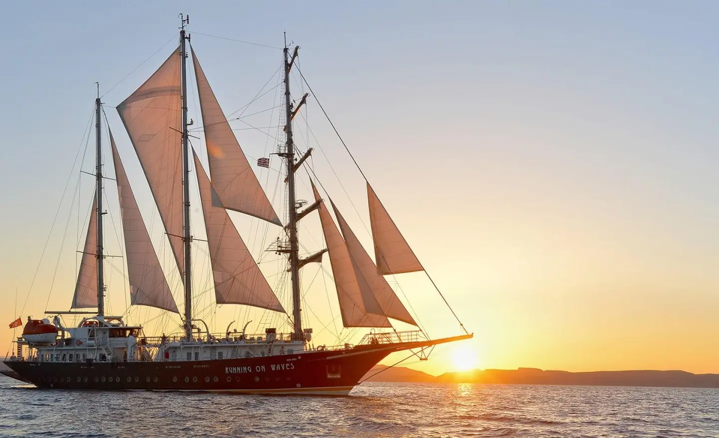 Gulet yacht named Running on Waves sails at sunset with orange sky