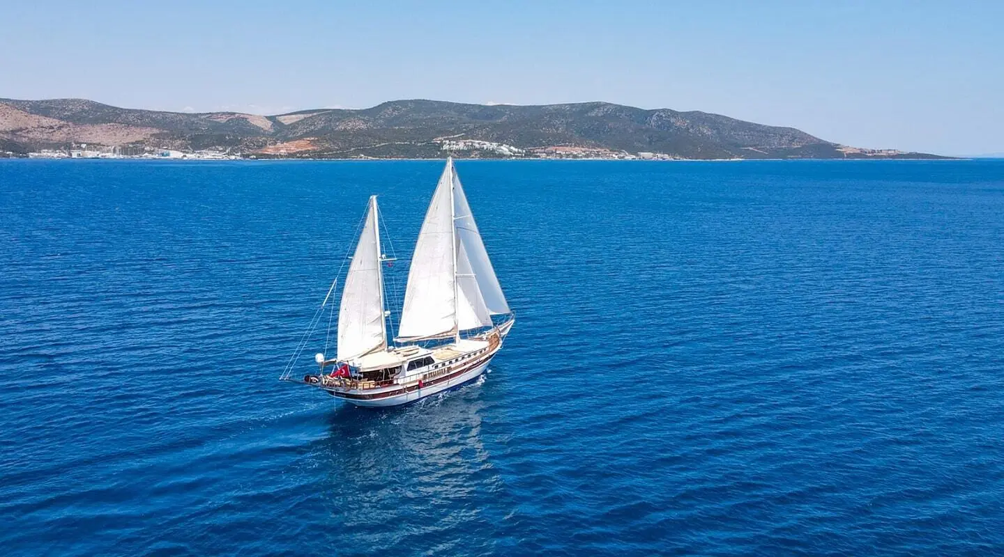 Two sailing yachts on blue sea with white sails, distant coastline