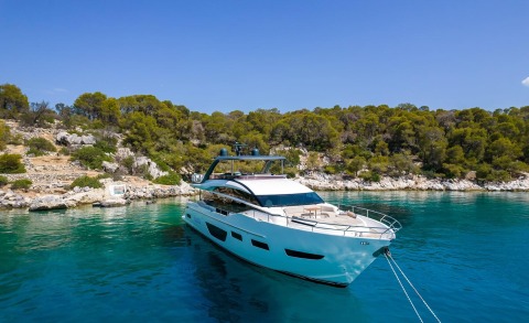 Vista yacht anchored in turquoise water with a rocky tree-covered shoreline in the background