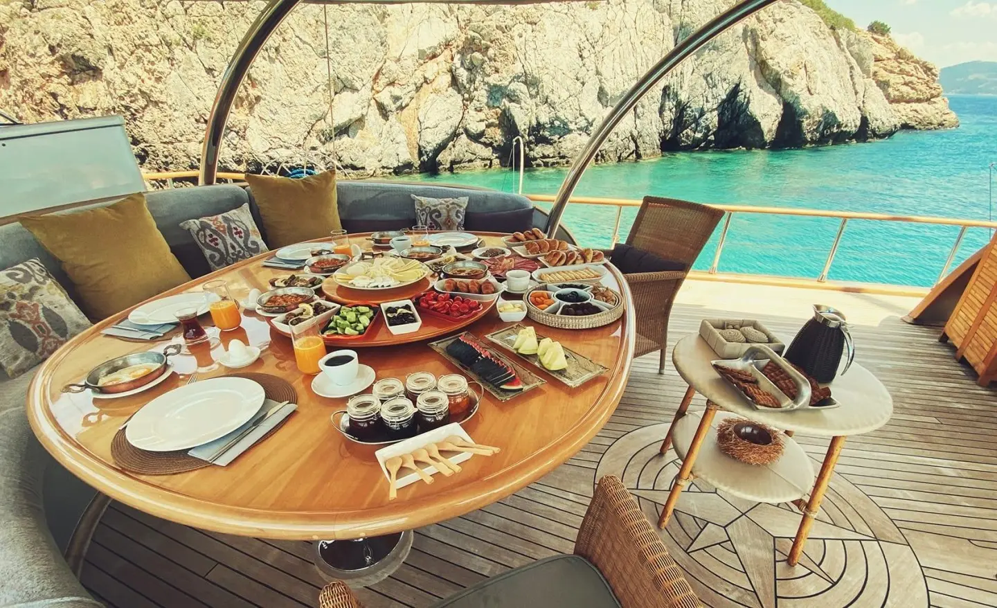 Silver Moon yacht anchored by rocky coast with a round wooden table set for dining at sunset