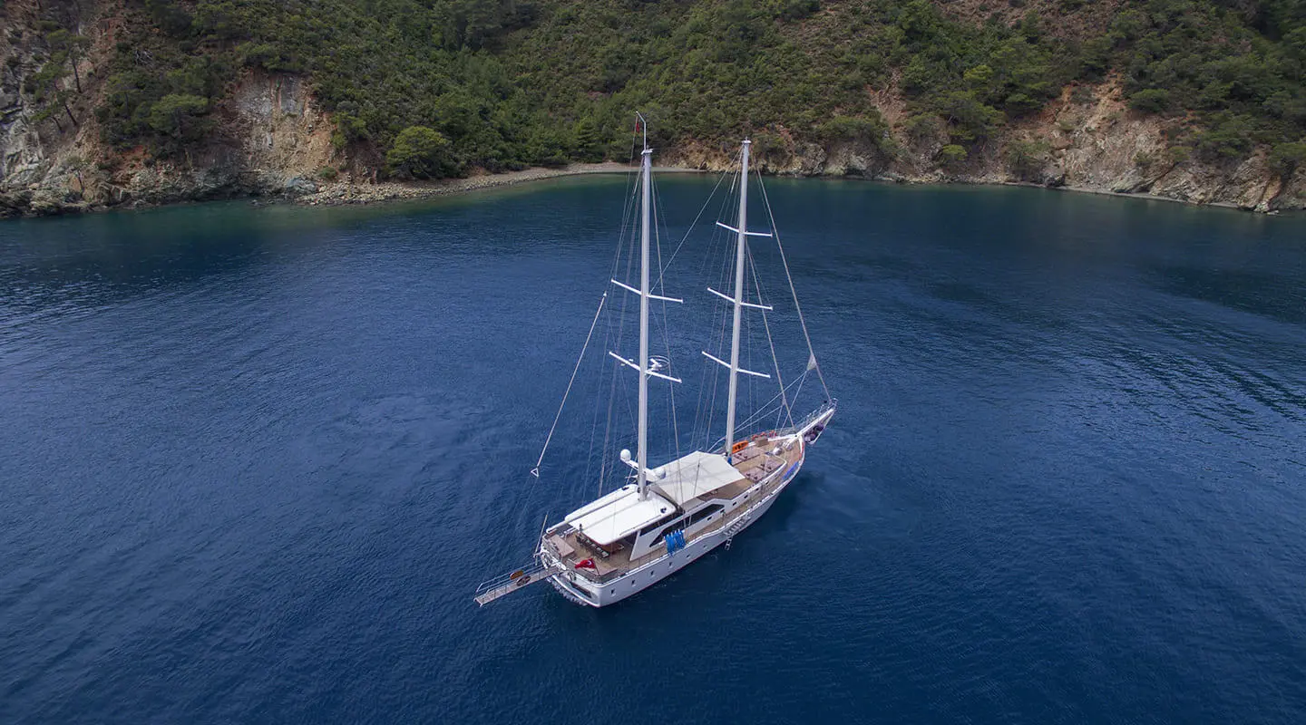 Anchored sailing yacht in calm blue sea near rocky coastline
