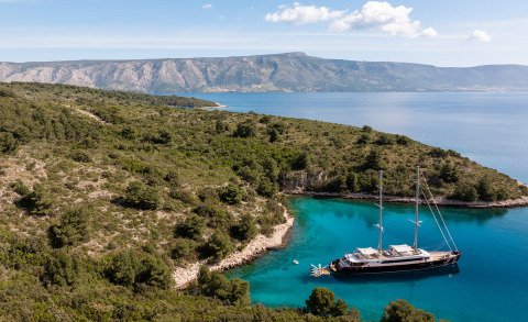 Nocturno yacht anchored in turquoise bay with rocky coastline and distant mountains