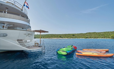 Rear view of La Perla yacht with open sea and shoreline in the background, inflatable water toys and a small deck seating area