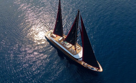 Aerial view of Anetta yacht with dark maroon sails cruising on blue sea
