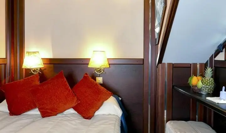 Yacht cabin bed with white sheets and red pillows, wooden headboard