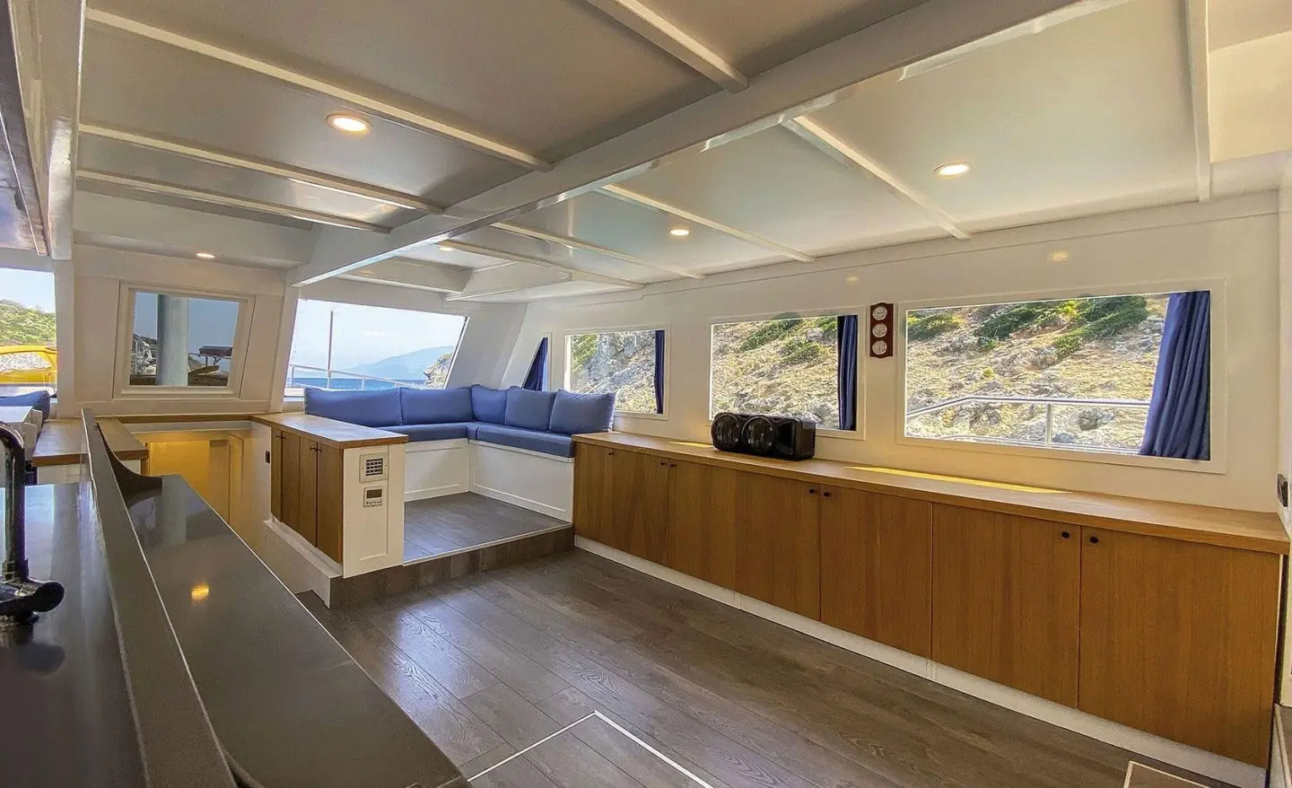 Maske 5 yacht interior with wooden deck, seating, and large windows at sunset