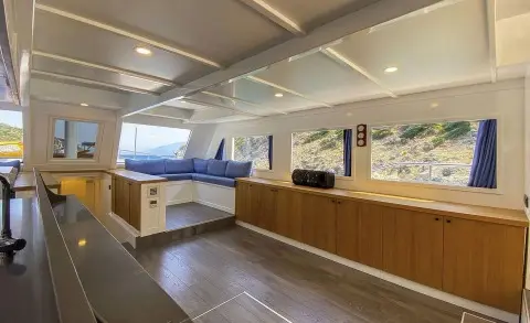 Maske 5 yacht interior with wooden deck, seating, and large windows at sunset