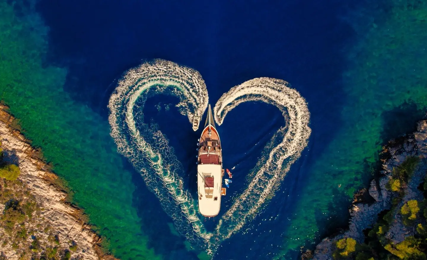 A luxury gulet Cesarica sails at sunset viewed from above, two curved masts framing the deck
