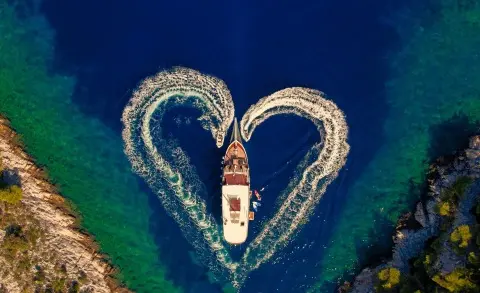 A luxury gulet Cesarica sails at sunset viewed from above, two curved masts framing the deck