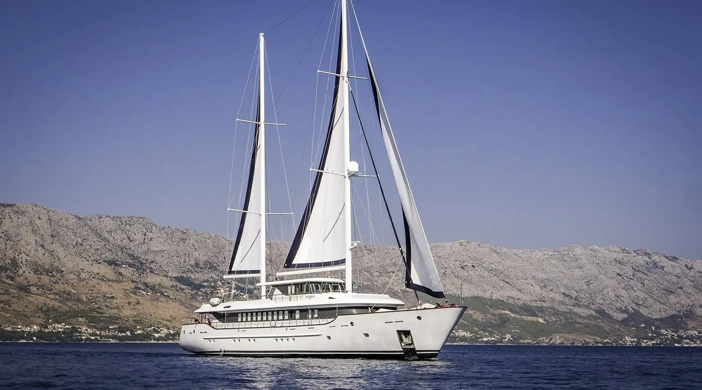 Omnia luxury yacht sailing near rocky coastline under clear blue skies
