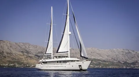 Omnia luxury yacht sailing near rocky coastline under clear blue skies