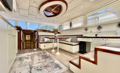 Interior of Derya Deniz yacht with corner seating, round table, white cabinets, windows letting in light, decorative plants