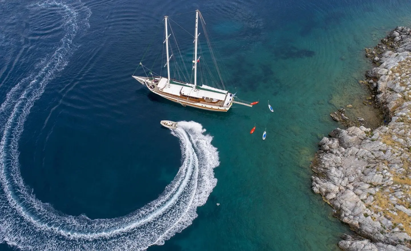 Ecce Navigo yacht gliding near rocky coastline at sunset with sails down