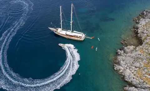 Ecce Navigo yacht gliding near rocky coastline at sunset with sails down