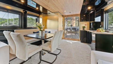 Interior dining area with white upholstered chairs around a dark table, glass doors to an outdoor deck in the background