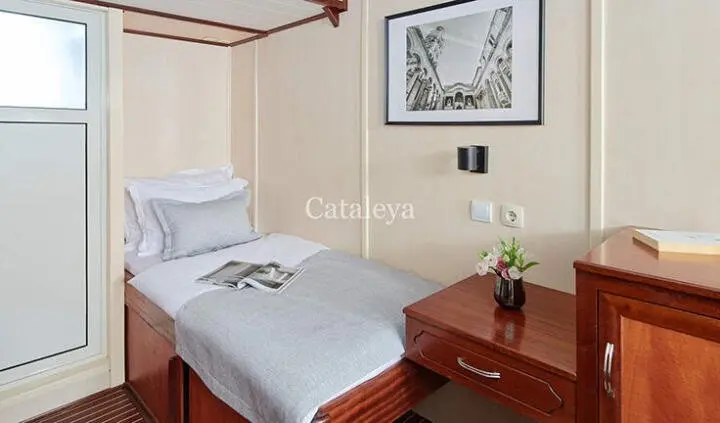 Two single beds with white bedding and a wooden bedside table in a cabin on a yacht