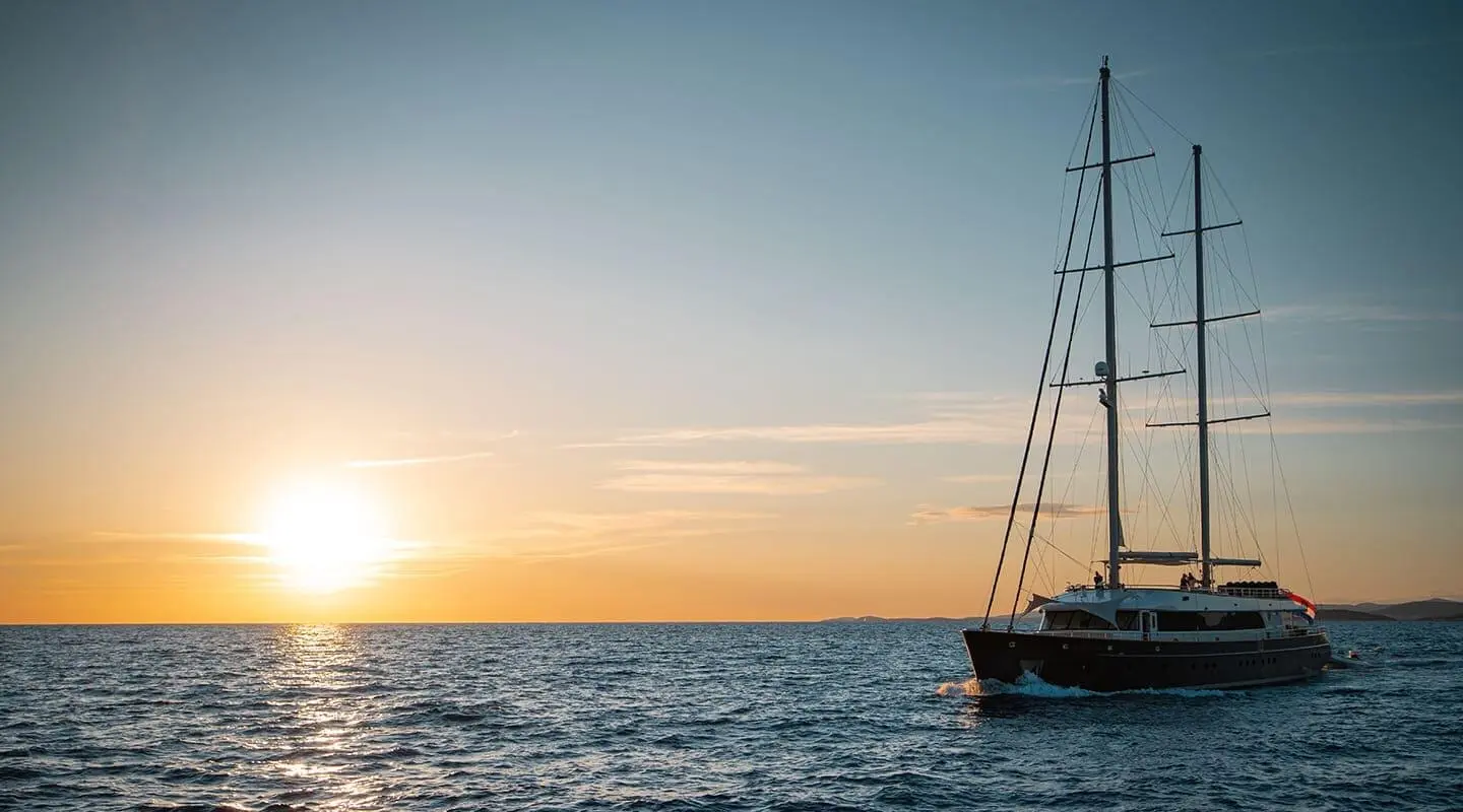 Dalmatino yacht at sunset with sailboat and calm sea reflections