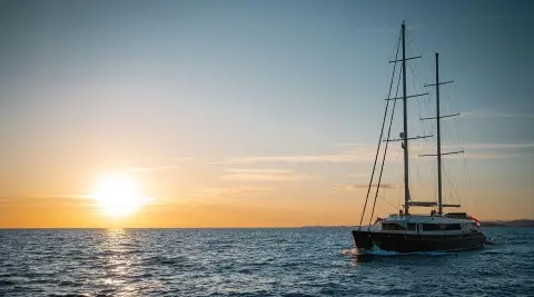 Dalmatino yacht at sunset with sailboat and calm sea reflections