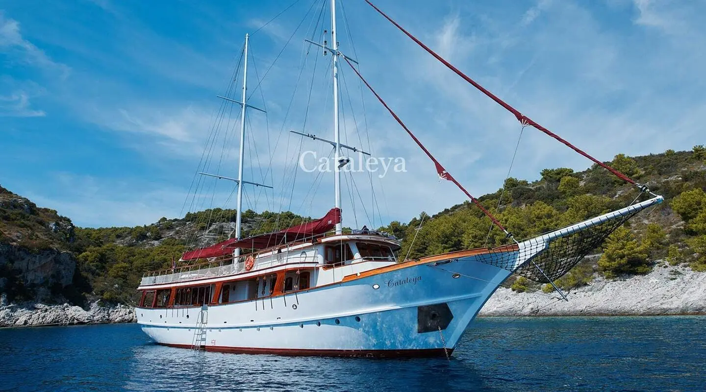 Cataleya yacht anchored near rocky coastline at sunset with blue sky