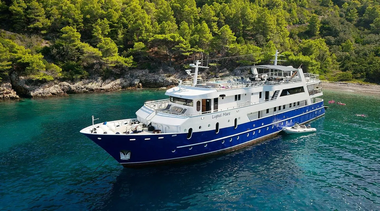 Lupus Mare yacht anchored near a forested coastline at sunset